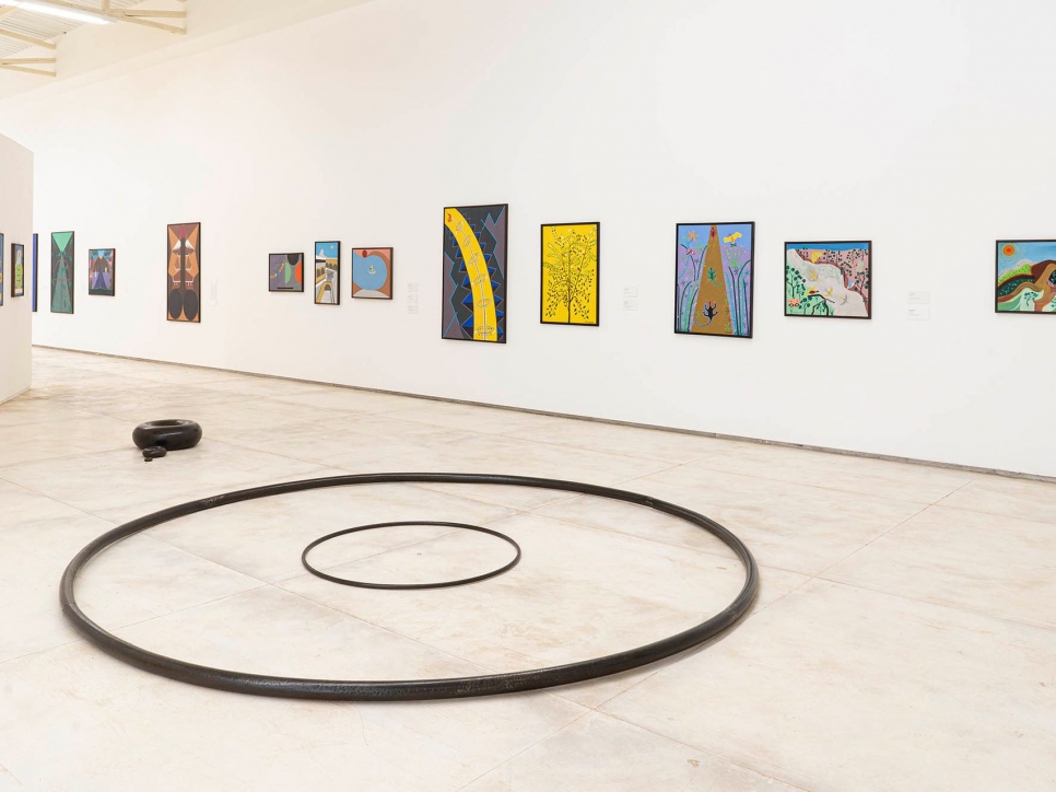 Gallery installation shot of paintings on wall and circle sculptures on floor